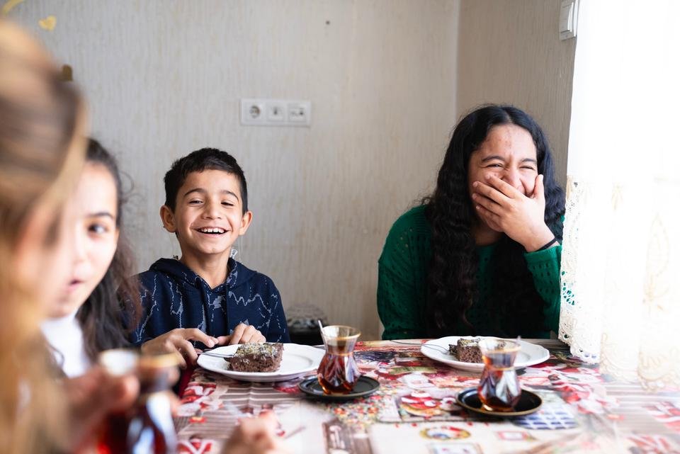 Siblings Cihan*, 11, Yasemin*, 13 and Hilal*, 16 enjoy a dessert made by their mother Tülay* at home in Gaziantep, Türkiye